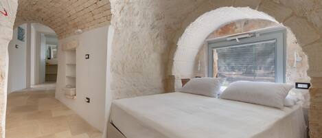 A bedroom with a stone wall, a bed, a window, and a door leading to another room.