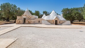 A building with multiple conical roofs and stone walls, surrounded by a gravel area and trees. - 3565 A Piedi Scalzi nel Trullo by Perle di Puglia (Latiano)