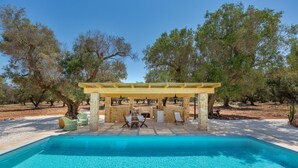 A pool area with a pergola, outdoor seating, and trees in the background. - 3565 A Piedi Scalzi nel Trullo by Perle di Puglia (Latiano)