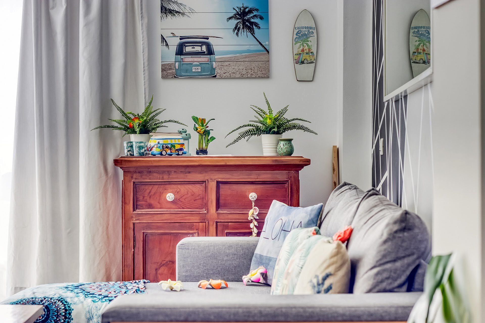 Un salon avec un canapé gris, un meuble en bois orné de plantes et un tableau sur le thème de la plage accroché au mur.