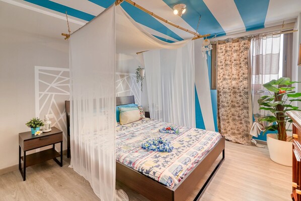 A bedroom with a bed, a nightstand, a potted plant, and a window with curtains.