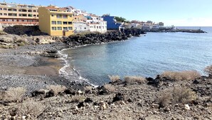 Una zona costera con edificios a lo largo de la playa, terreno rocoso y cielo despejado.