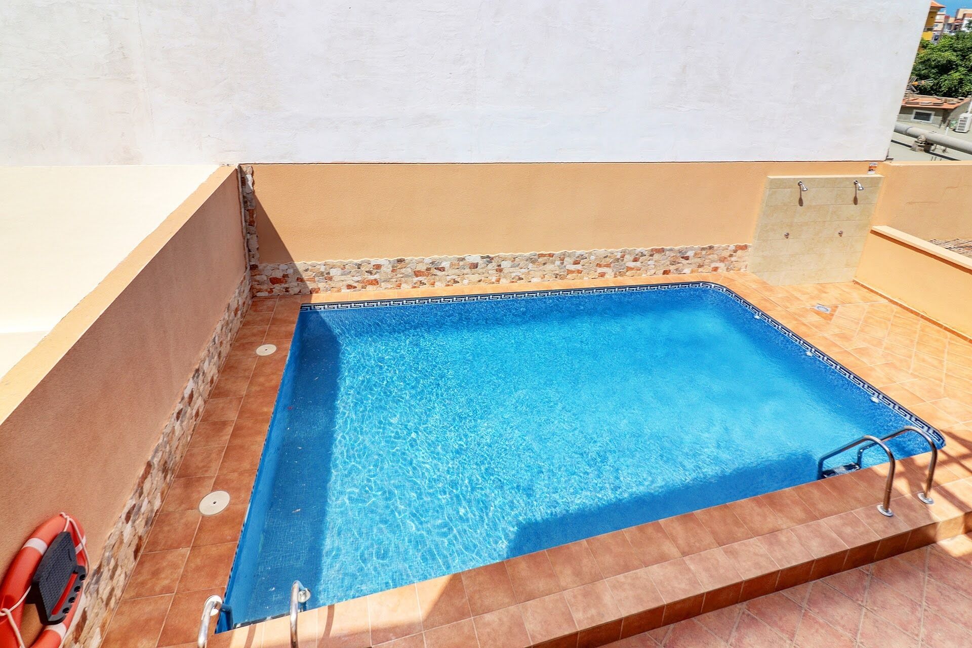A rectangular swimming pool with a blue interior, surrounded by a tiled deck and a stone border.