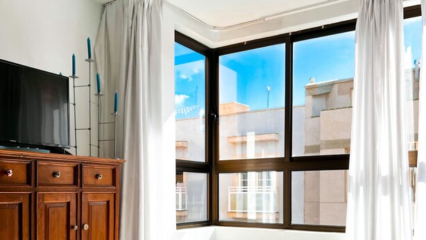 Una habitación con un ventanal grande, un armario de madera y un cuenco con conchas marinas en el suelo.