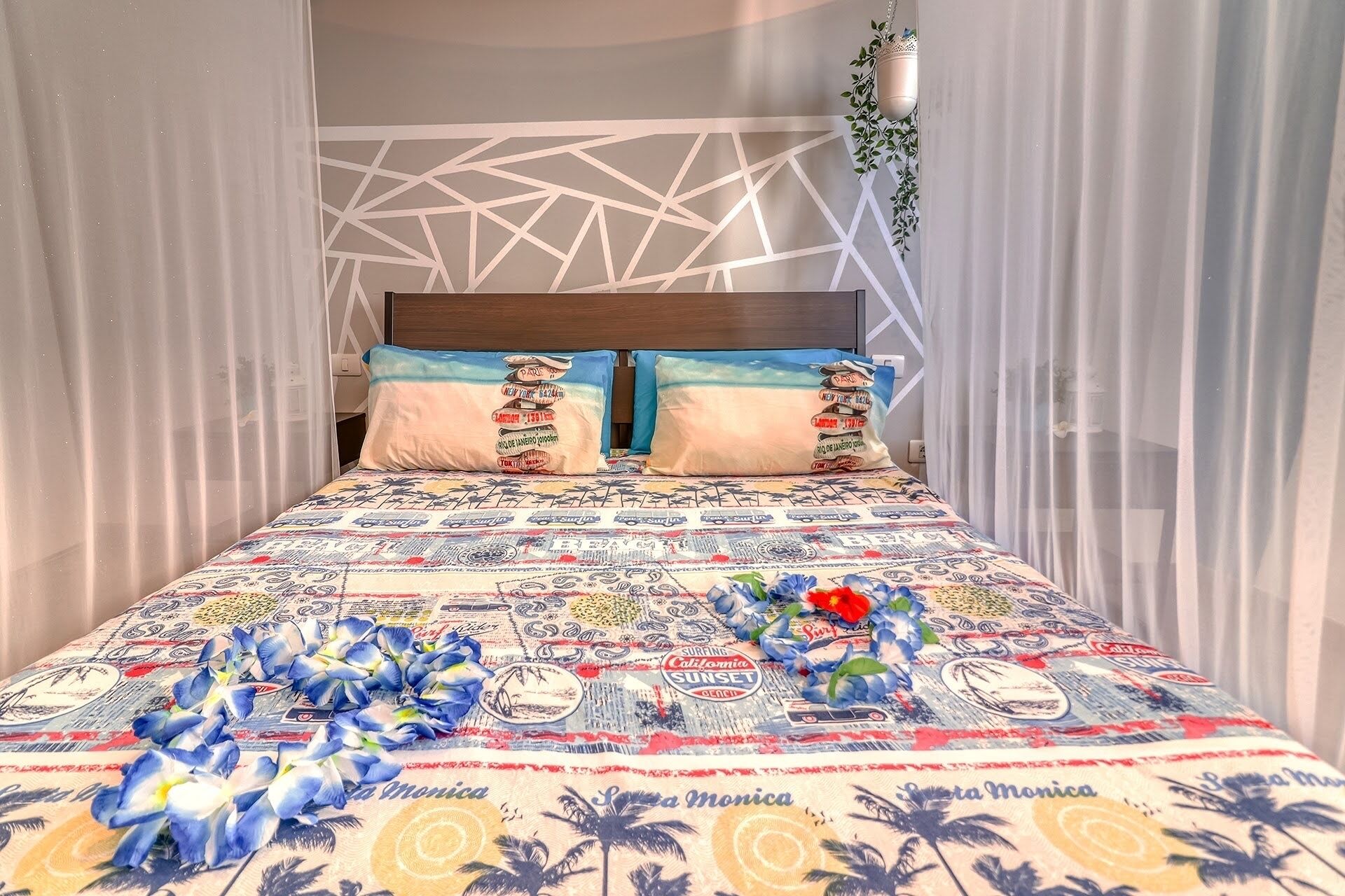 A bed with a patterned bedspread, two pillows with travel-themed designs, and a decorative plant.