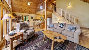 A spacious living area with a high ceiling, wooden beams, a sofa, a coffee table, and a staircase leading to an upper level.