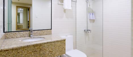 A bathroom with a granite countertop sink, a white toilet, a glass-enclosed shower, and a towel rack with towels.