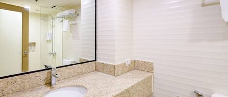 A modern bathroom with a granite countertop sink, a large mirror, and a shower area.