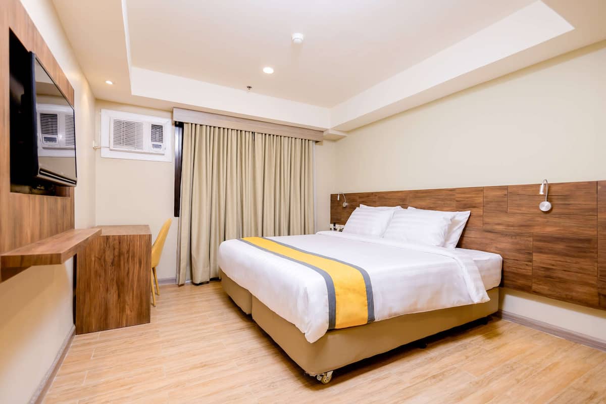 Ein Hotelzimmer mit einem großen Bett, einem Holz-Kopfteil, einem flachbildfernseher an der Wand, einem Schreibtisch und einem Stuhl.