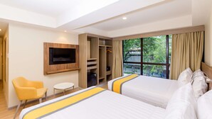 Une chambre d’hôtel avec deux lits, un téléviseur fixé au mur, une armoire, une petite table et une chaise.