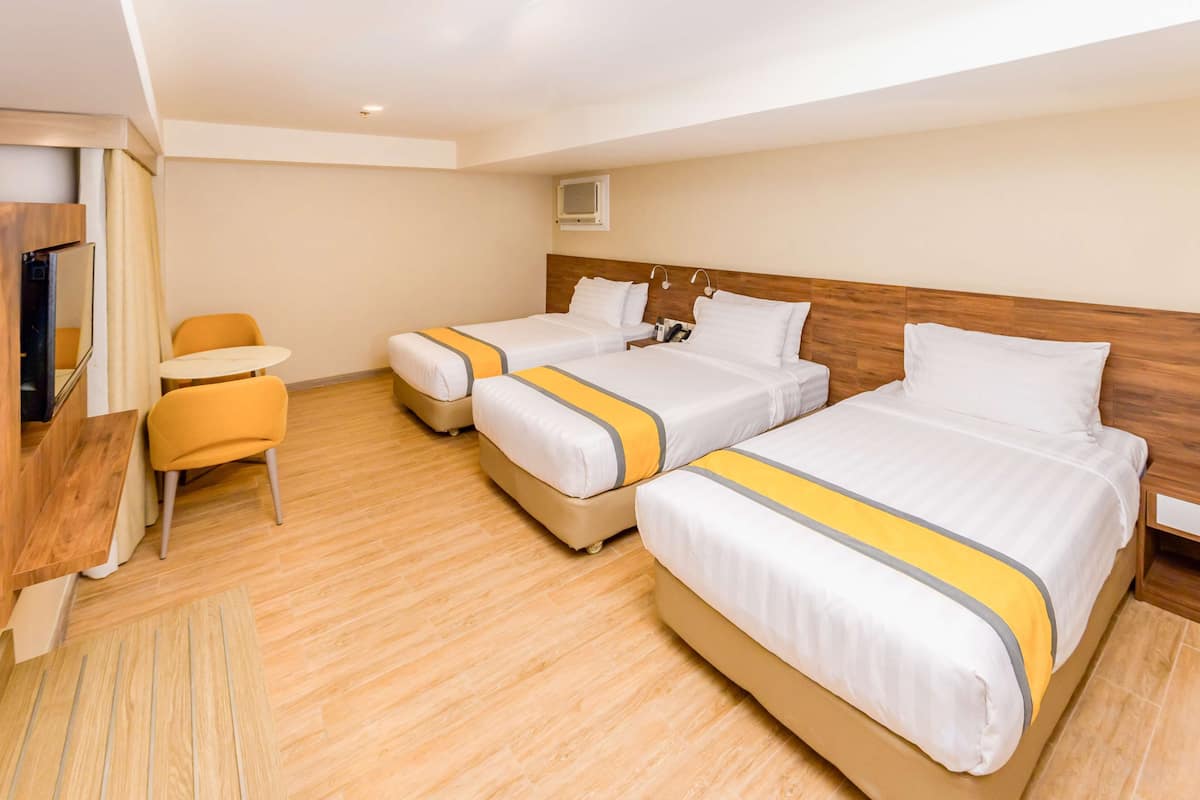 Ein Hotelzimmer mit zwei Betten, einem kleinen Tisch, einem Sessel und einem Fernseher.
