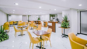 Un espace repas moderne avec des chaises et des tables jaunes, un comptoir d’accueil et des plantes en pot.