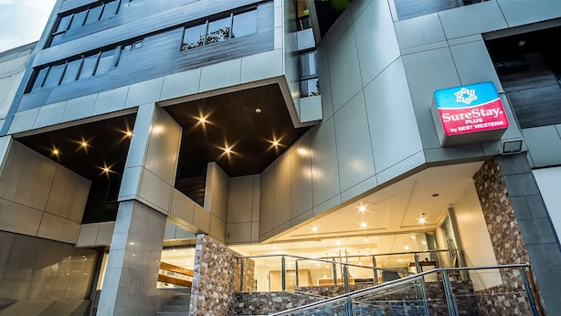 Une entrée d’hôtel moderne avec une façade en verre, un escalier doté de rampes en métal et une enseigne indiquant « SureStay by Best Western ».