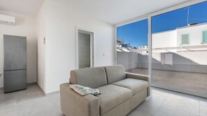A modern living room with a beige sofa, a small table, and a sliding glass door leading to a balcony. - 3399 Bina House by Barbarhouse (Carovigno)