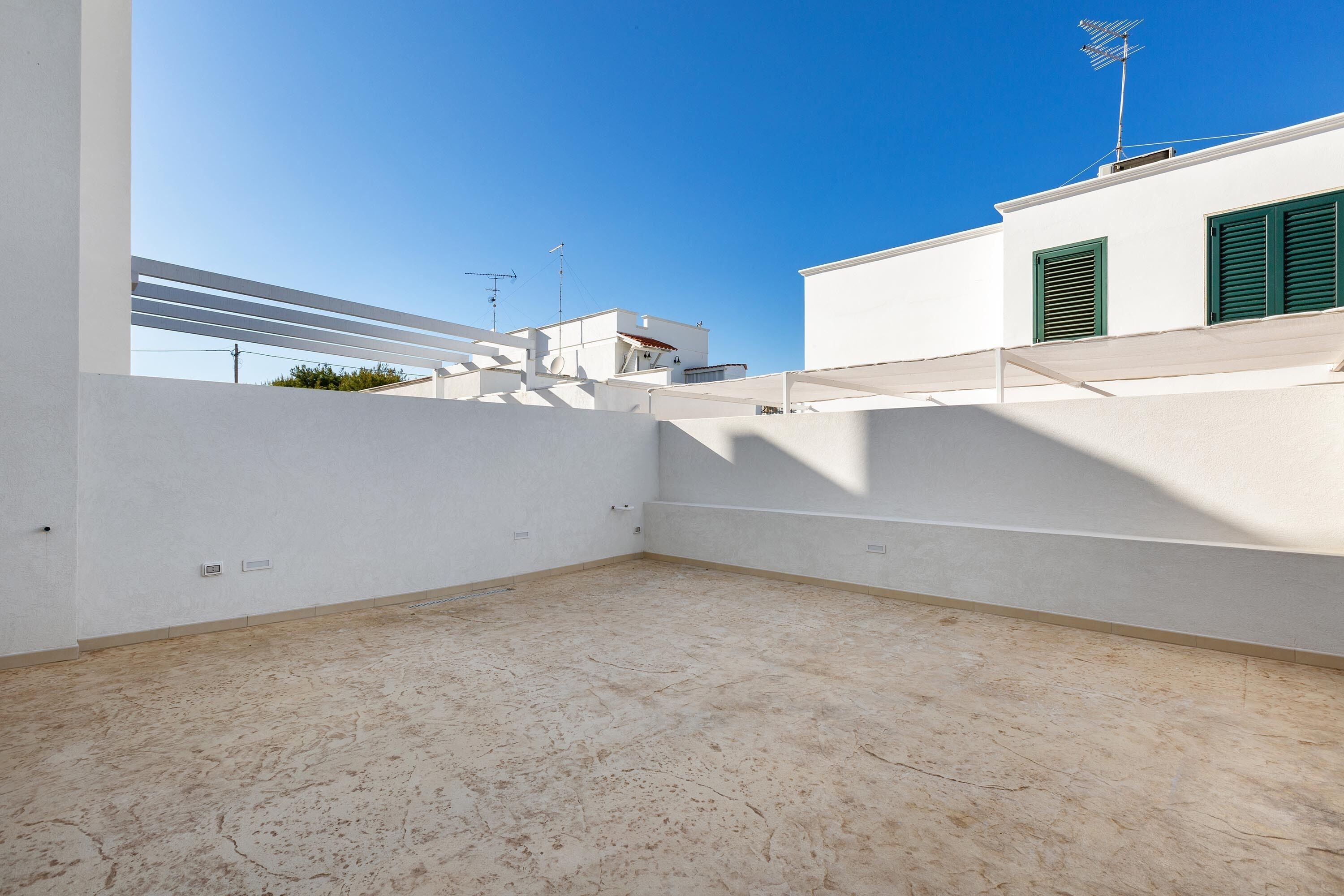 Terraço no telhado com céu azul claro, paredes brancas e persianas verdes.