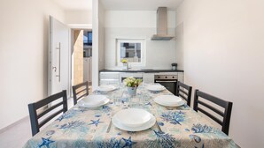 A dining area with a table set for four, a kitchen in the background, and a door leading to another room. - 3399 Bina House by Barbarhouse (Carovigno)