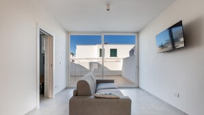 A modern living room with a sofa, a flat-screen TV mounted on the wall, and a large sliding glass door leading to an outdoor balcony. - 3399 Bina House by Barbarhouse (Carovigno)