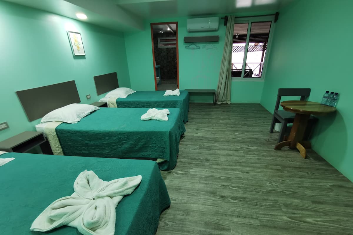 Habitación de hotel con tres camas, cada una con una toalla, una mesita y una silla.