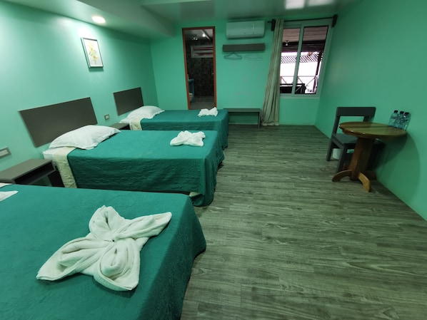 Habitación de hotel con tres camas, cada una con una toalla, una mesita y una silla.