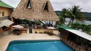 A pool area with a thatched-roof structure, outdoor seating, and a view of the water.