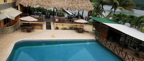 Un área de piscina con una estructura de techo de paja, asientos al aire libre y vista al agua.