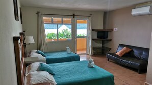 A hotel room with two beds, a sofa, a TV, and a view of greenery outside.
