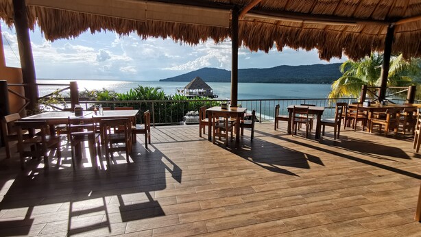 A wooden deck with tables and chairs, overlooking a lake with mountains in the background.
