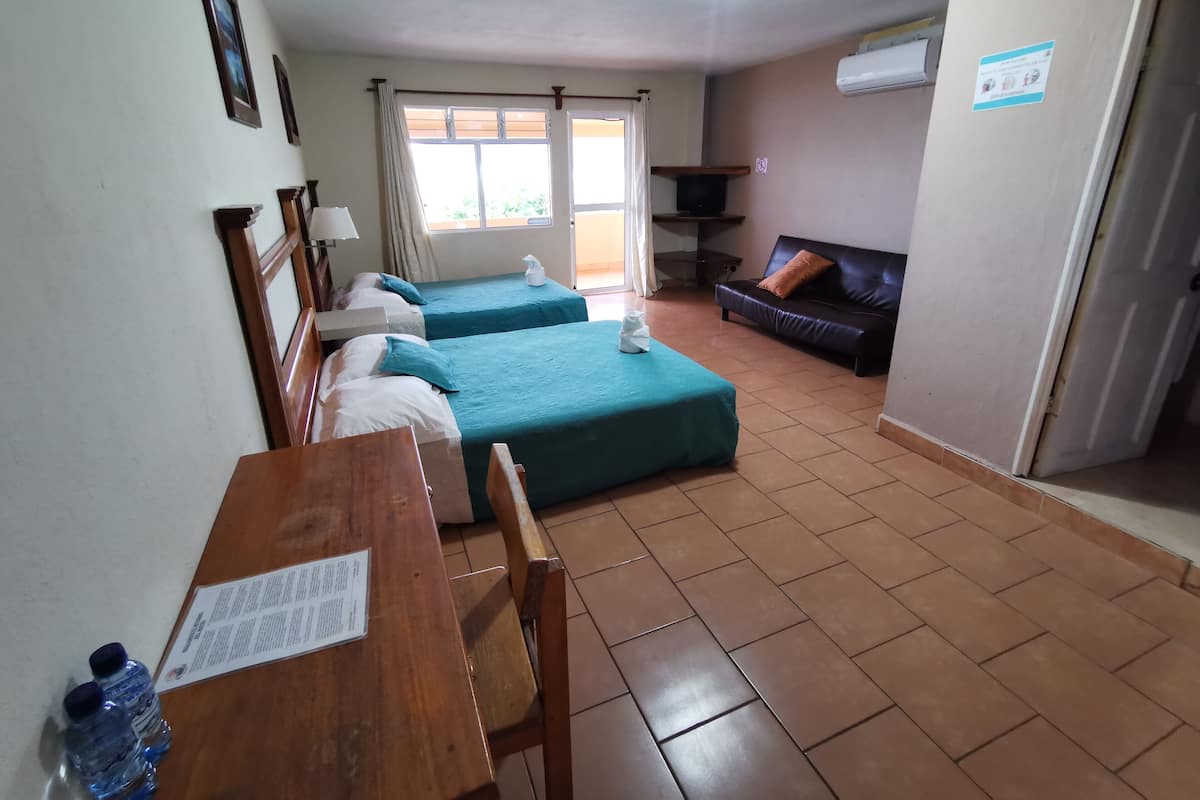 Una habitación de hotel con dos camas, una mesa de madera con un menú, una televisión y un sofá.