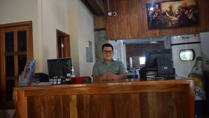A wooden reception desk with a computer, a cash register, and a bottle of hand sanitizer.