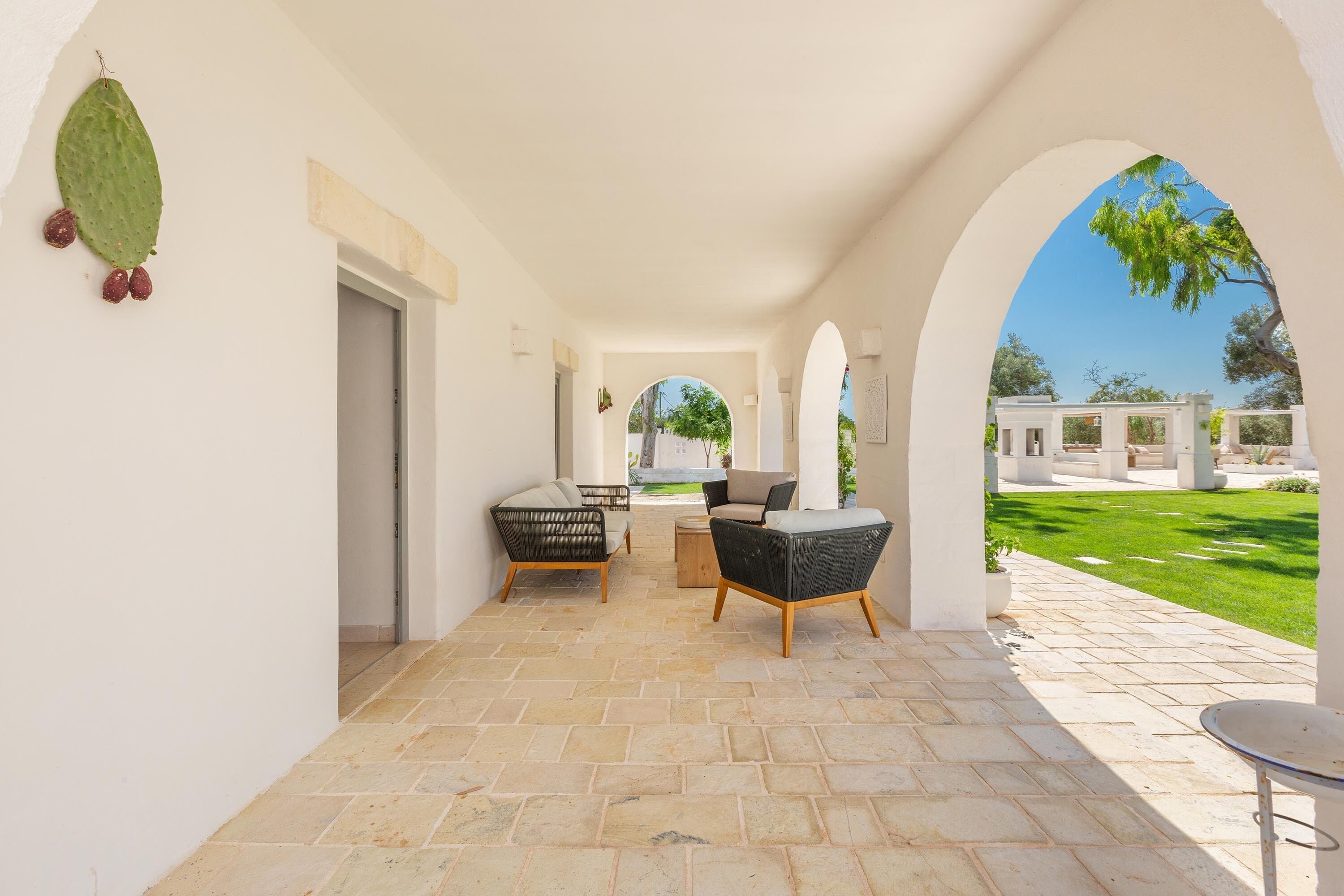 A covered outdoor seating area with stone flooring, two sofas, and a small table.