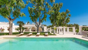A swimming pool with lounge chairs, surrounded by trees and a white building with arches. - 3589 Borgo Treffe by Perle di Puglia (Ostuni)