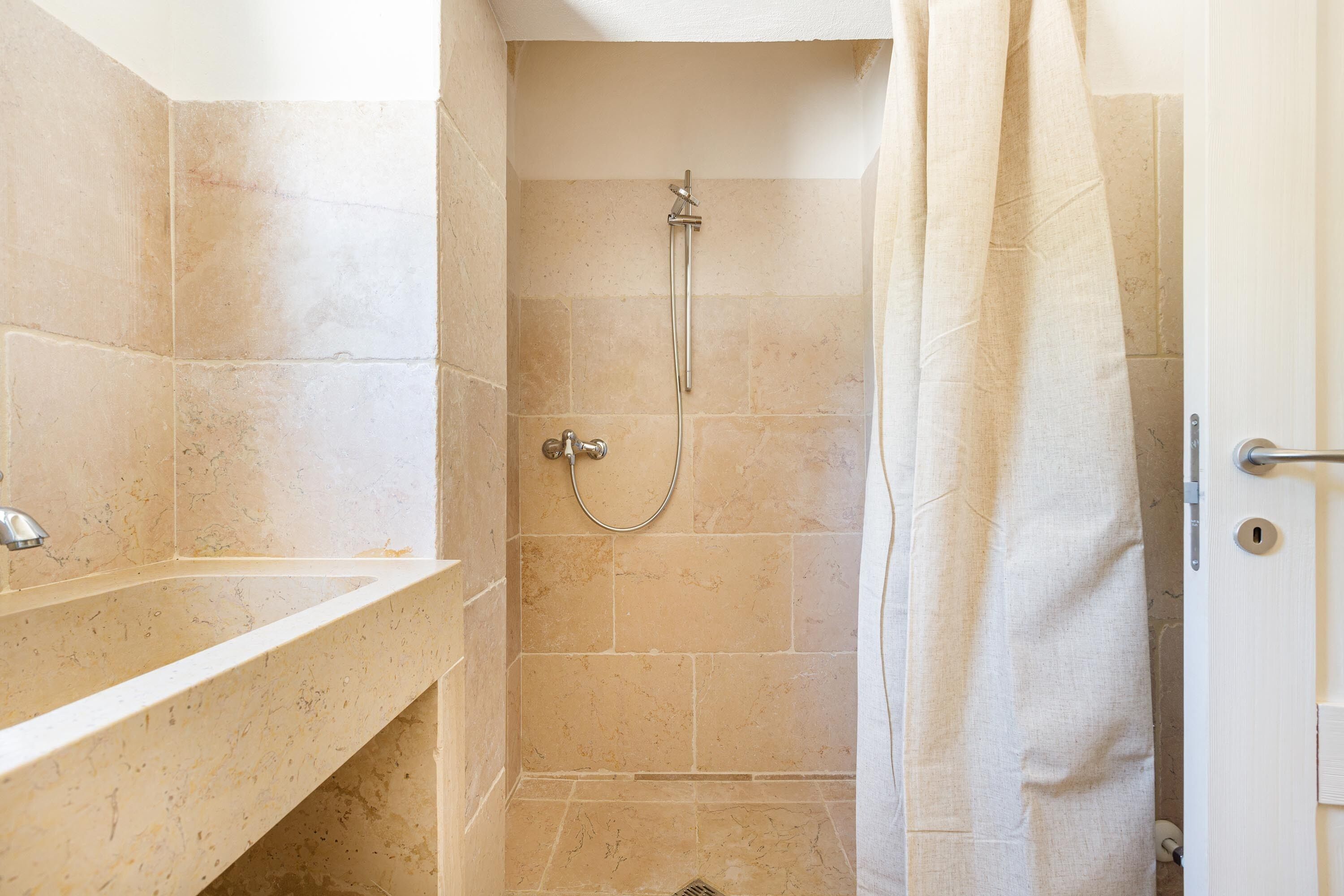 A bathroom with beige tiles, a shower, and a sink.