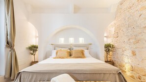 A bedroom with a large bed, a wooden bench, and a stone wall. - 3589 Borgo Treffe by Perle di Puglia (Ostuni)