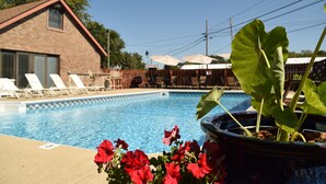 A swimming pool with lounge chairs, a brick building, and a potted plant with red flowers. - Steps to Lake Erie near Lakeside & Port Clinton - Private Hot Tub & Recreation (Lakeside Marblehead)