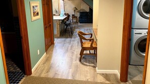 A laundry room with a washing machine, a dining area with wooden chairs, and a staircase leading to another level. - Steps to Lake Erie near Lakeside & Port Clinton - Private Hot Tub & Recreation (Lakeside Marblehead)
