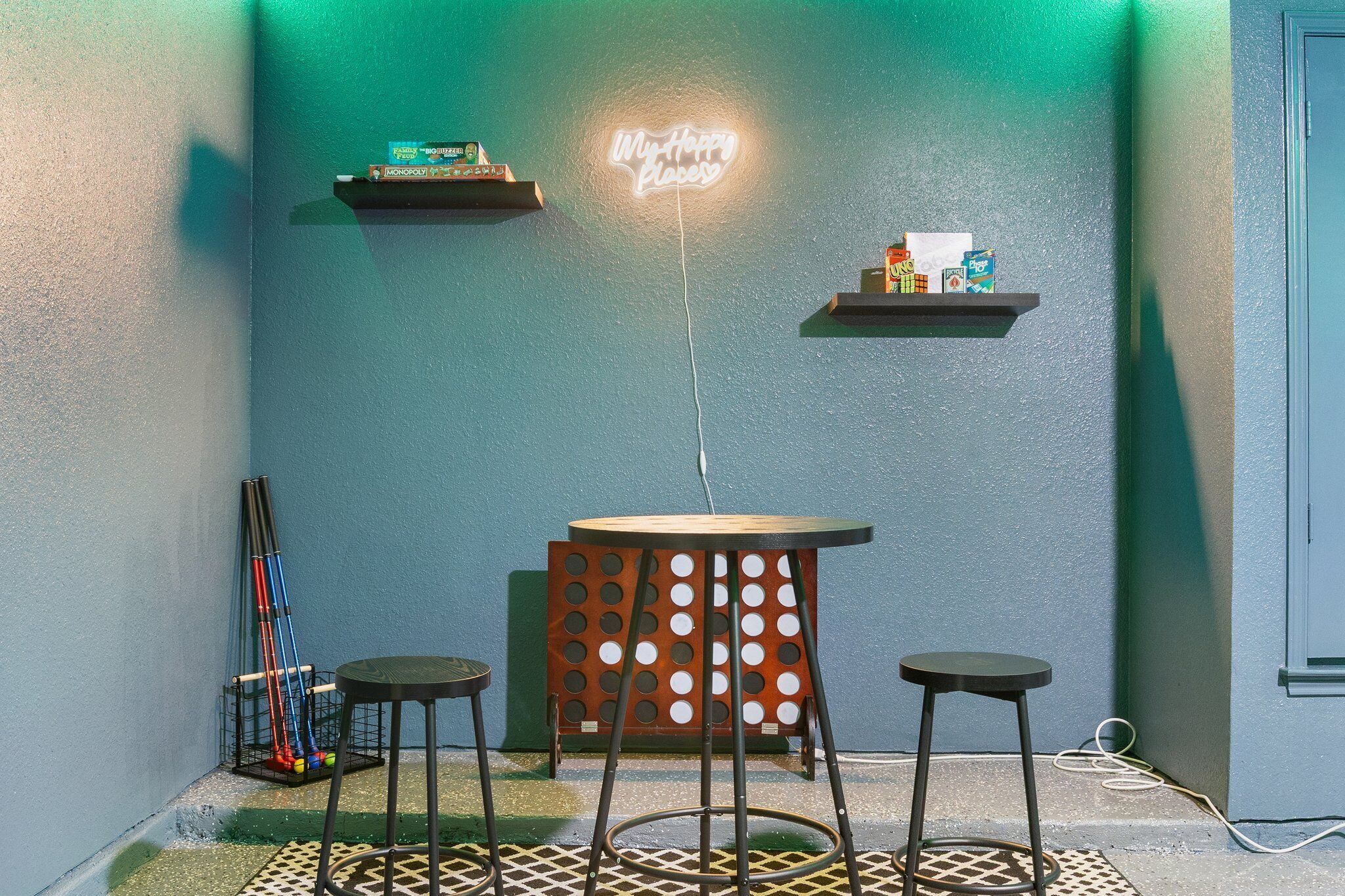 A corner with a neon sign, two tables, and shelves with items.