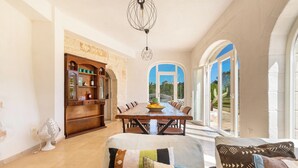 A spacious dining area with a wooden table and chairs, a built-in bookshelf, and a view through large arched windows. - 3483 Casale Amenola by Perle di Puglia (Ostuni)