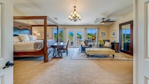 Une chambre spacieuse avec un lit à baldaquin, un coin repas et un espace détente comprenant un canapé et un pouf.
