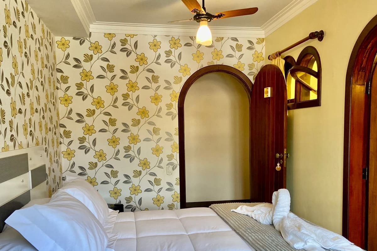 A bedroom with a bed, a ceiling fan, floral wallpaper, and wooden doors.