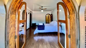 Un dormitorio con un arco de madera en la entrada, una cama, un ventilador de techo y una pequeña mesa con una silla.