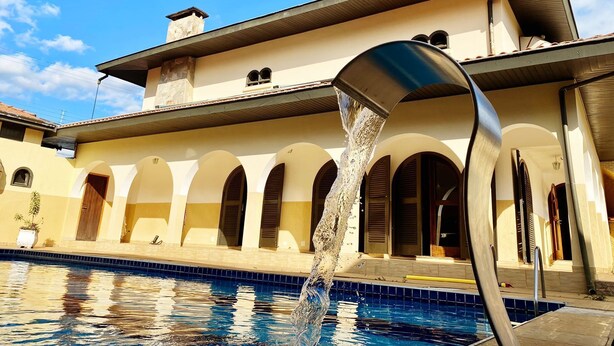 Una piscina con fuente, un edificio con arcos y cielo despejado.