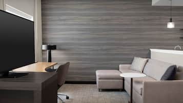 A modern hotel room with a flat-screen TV, a desk, a sofa, a small round table, and a lamp.