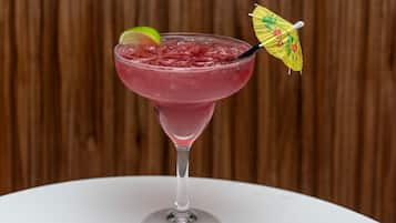 Un cocktail servi dans un verre à martini, décoré d’un petit parapluie sur le bord, avec des glaçons et une tranche de citron vert.