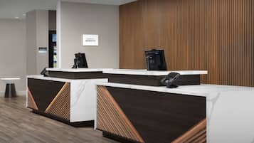A modern hotel reception area with two reception desks, a sign for the market, and a wooden panel wall.