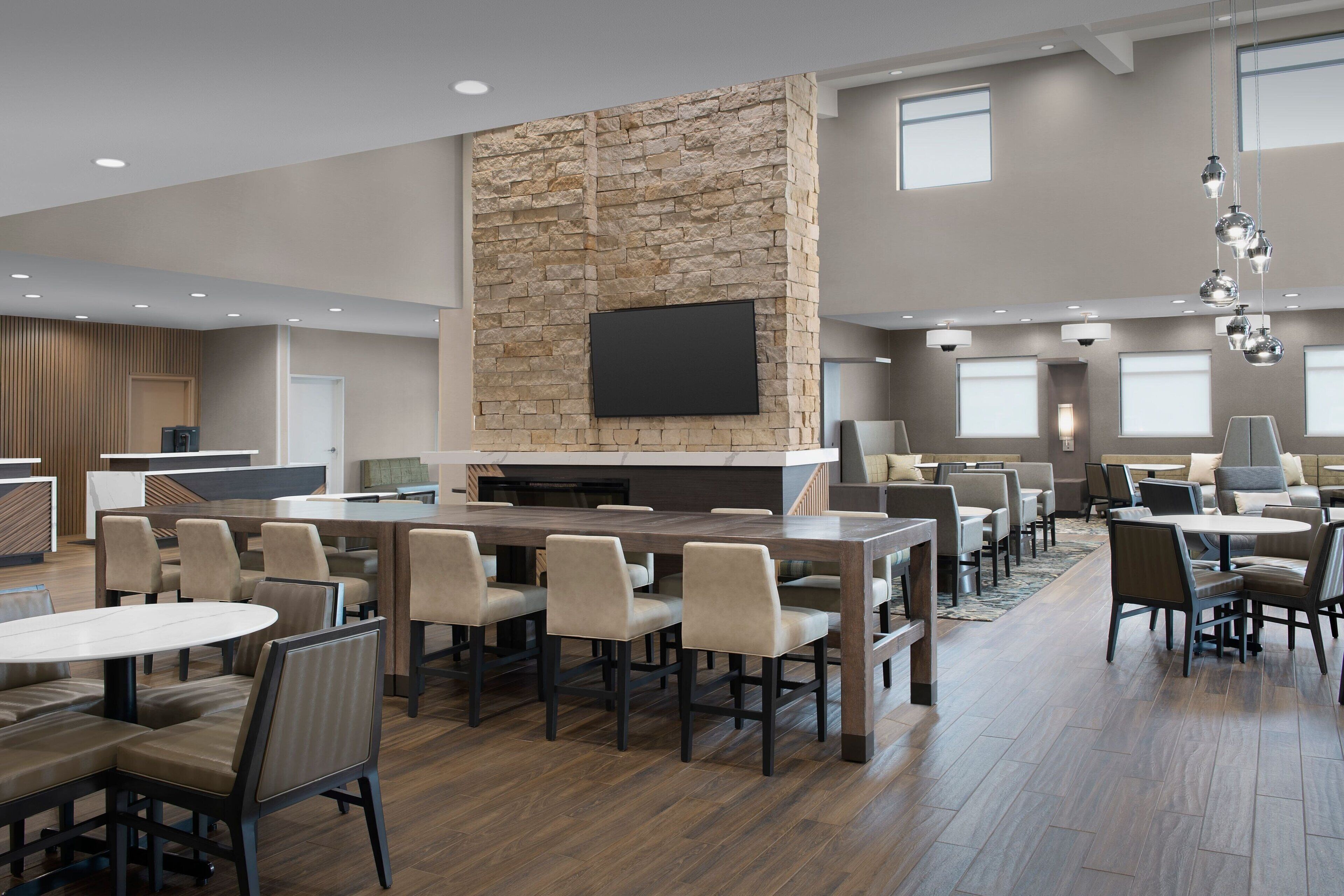 A modern indoor space with a stone accent wall, a flat-screen TV, and multiple seating areas with tables and chairs.
