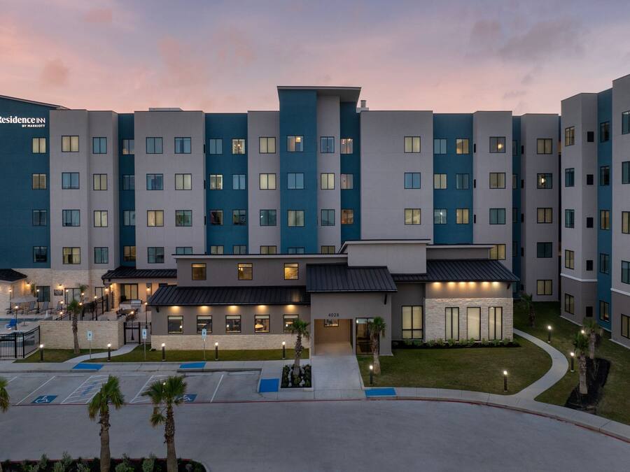 A multi-story hotel with a modern design, featuring a central entrance, a parking area, and a landscaped courtyard.