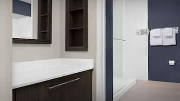 Une salle de bain moderne avec un meuble-lavabo en bois foncé, un plan de toilette blanc, une douche en verre et un mur d’accent bleu foncé.