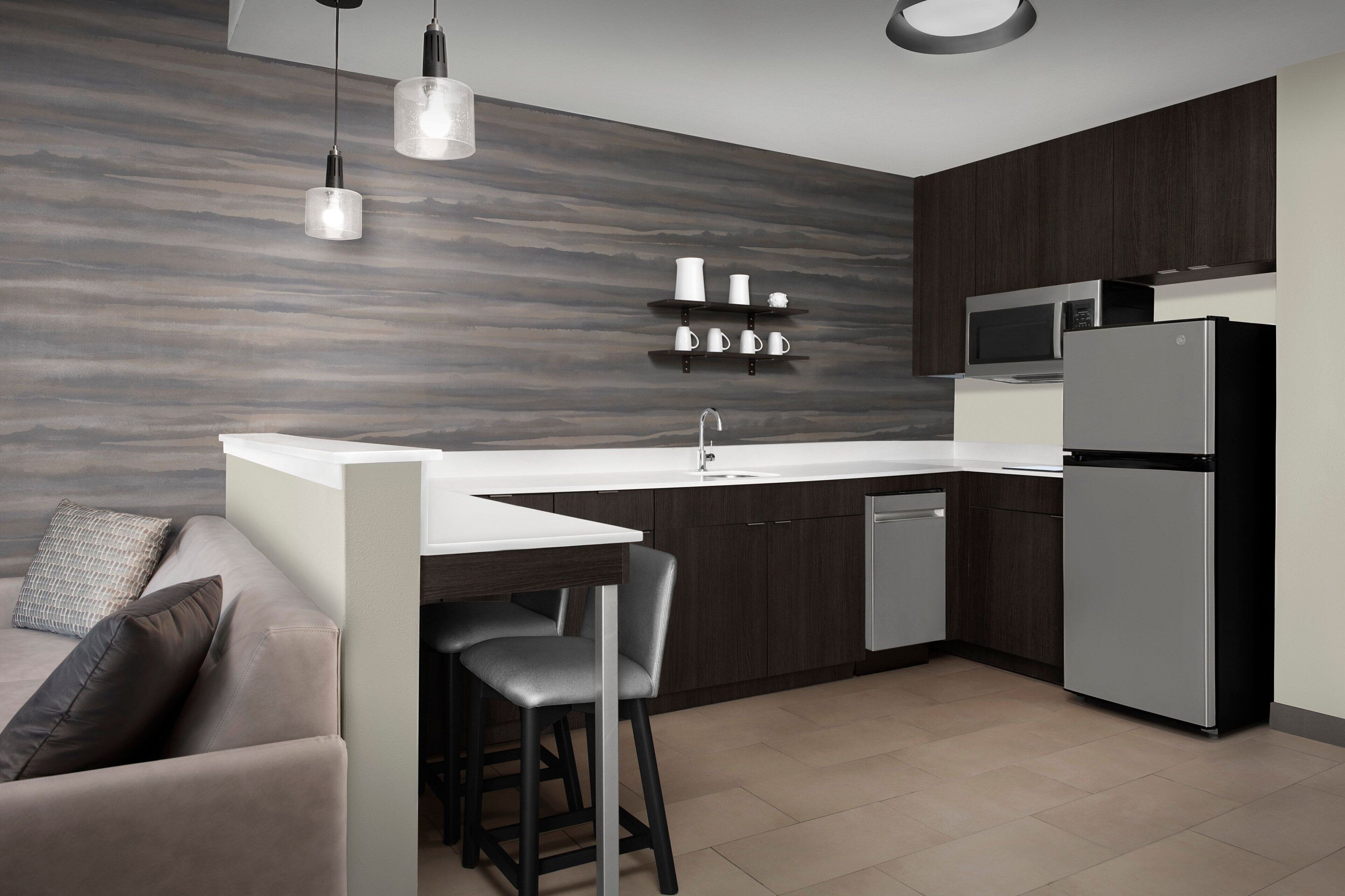 A modern kitchen with a white countertop, dark wooden cabinets, a built-in microwave, and a stainless steel refrigerator.