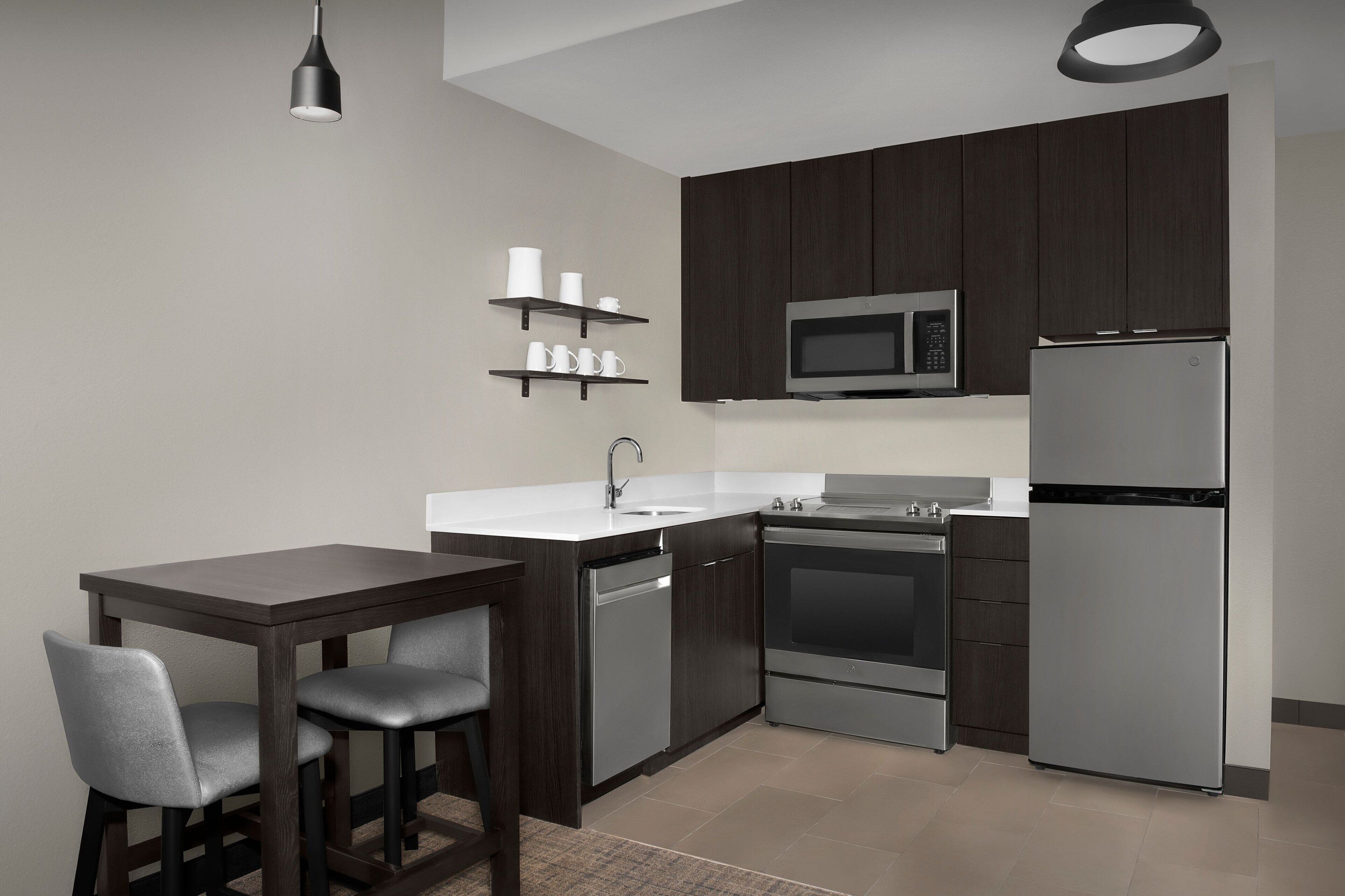 A modern kitchen with dark wooden cabinets, stainless steel appliances, a white countertop, and a bar stool.