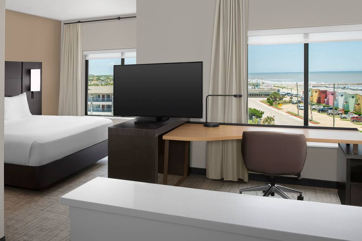 Ein Hotelzimmer mit Bett, Schreibtisch, Fernseher und Blick auf den Strand.